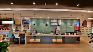 A modern reception area with two receptionists, a coffee bar, and a digital menu display. - ibis Xiamen Kaiyuan (Xiamen)