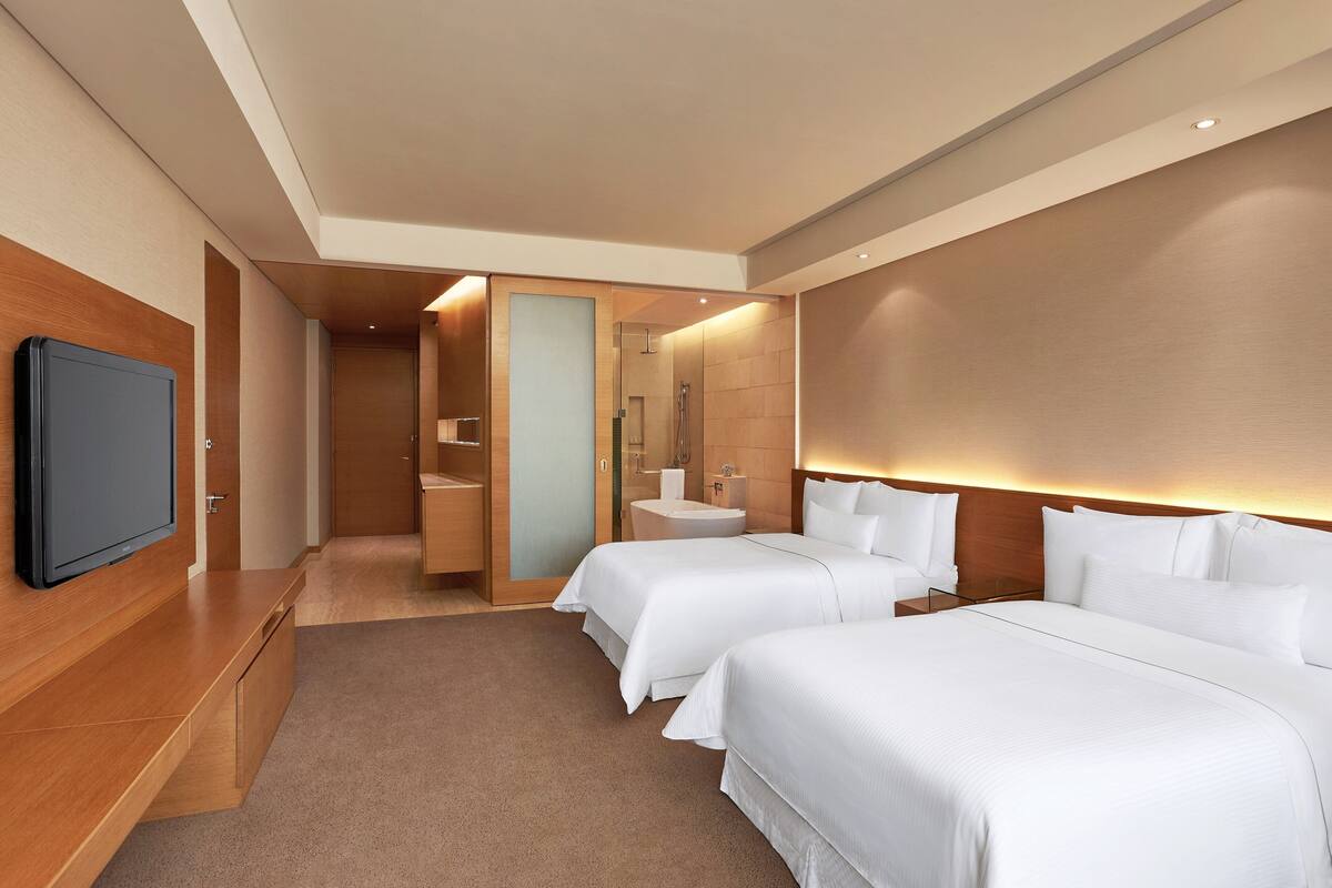 A modern hotel room with two beds, a TV, a bathroom, and a wooden wall.