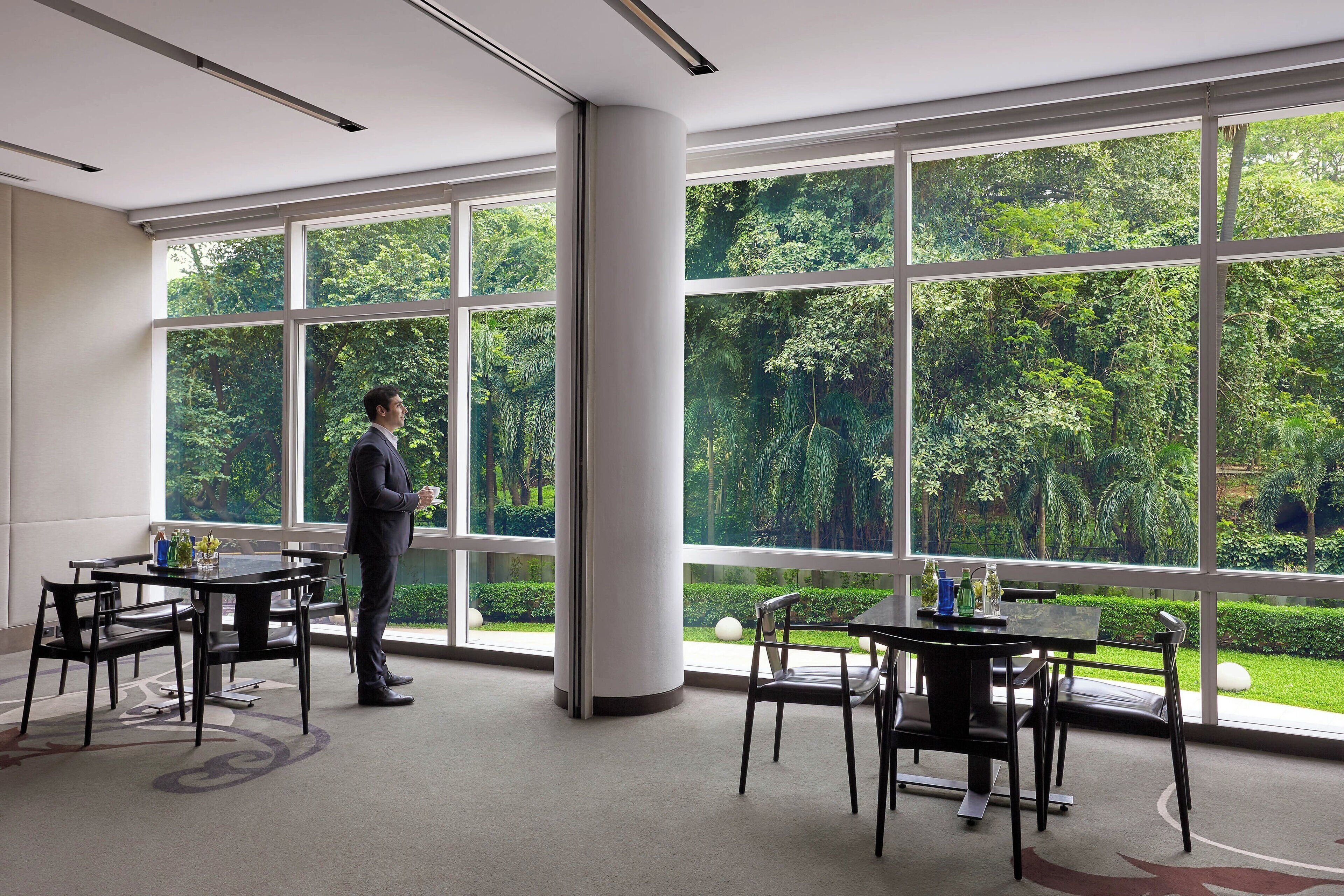 Una sala de conferencias moderna con ventanas amplias, un hombre de pie y una mesa con sillas.