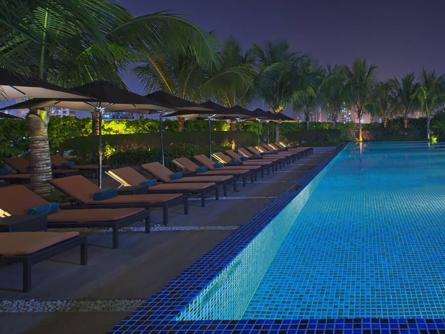 A poolside area with lounge chairs and umbrellas, surrounded by palm trees.