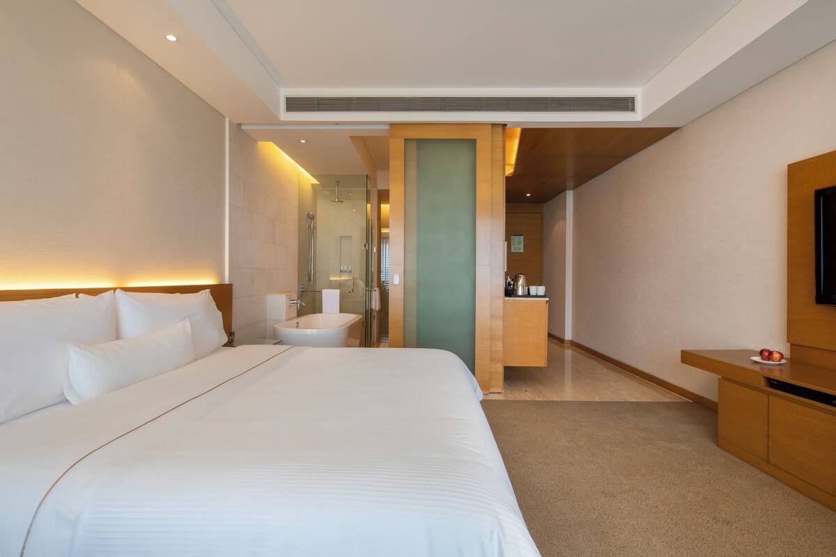 A modern hotel room with a large bed, a bathroom with a sink and mirror, and a wooden cabinet with a television.