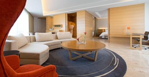 Una camera d'hotel moderna con un divano, un tavolino rotondo e una scrivania con una sedia.