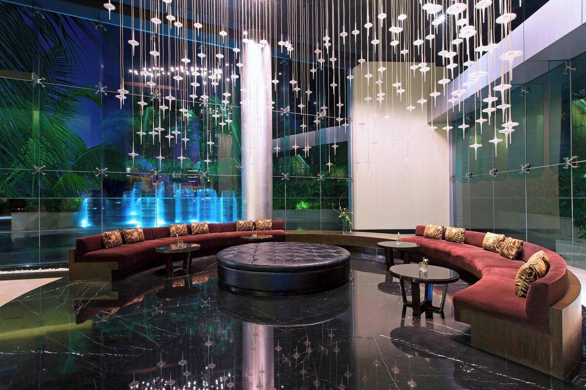 A modern lobby with a curved red sofa, a round black ottoman, and hanging light fixtures.