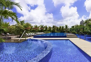 Piscina con piastrelle a mosaico blu, circondata da palme e sedie a sdraio.