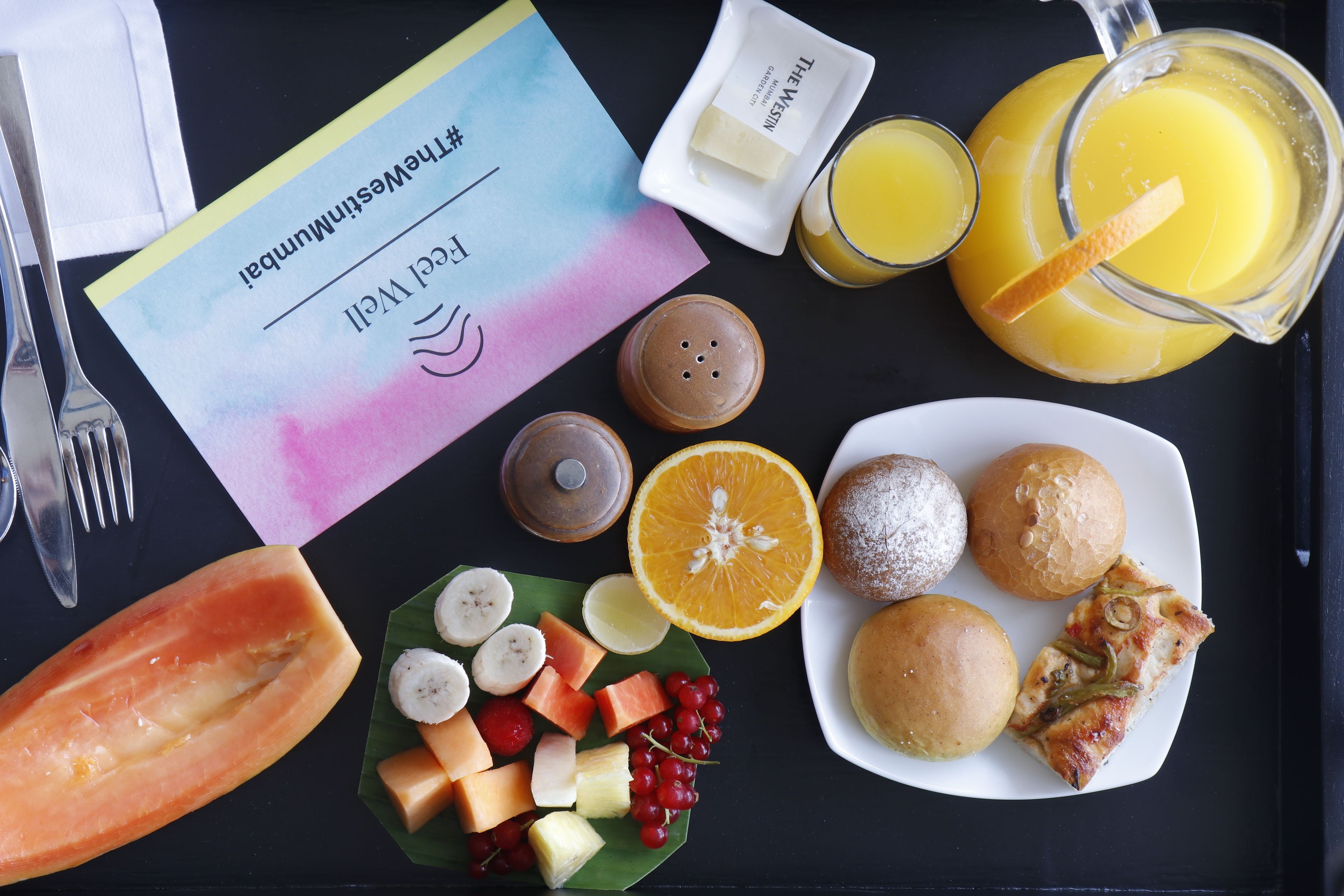 A breakfast tray with a variety of foods including bread, fruit, and a drink.