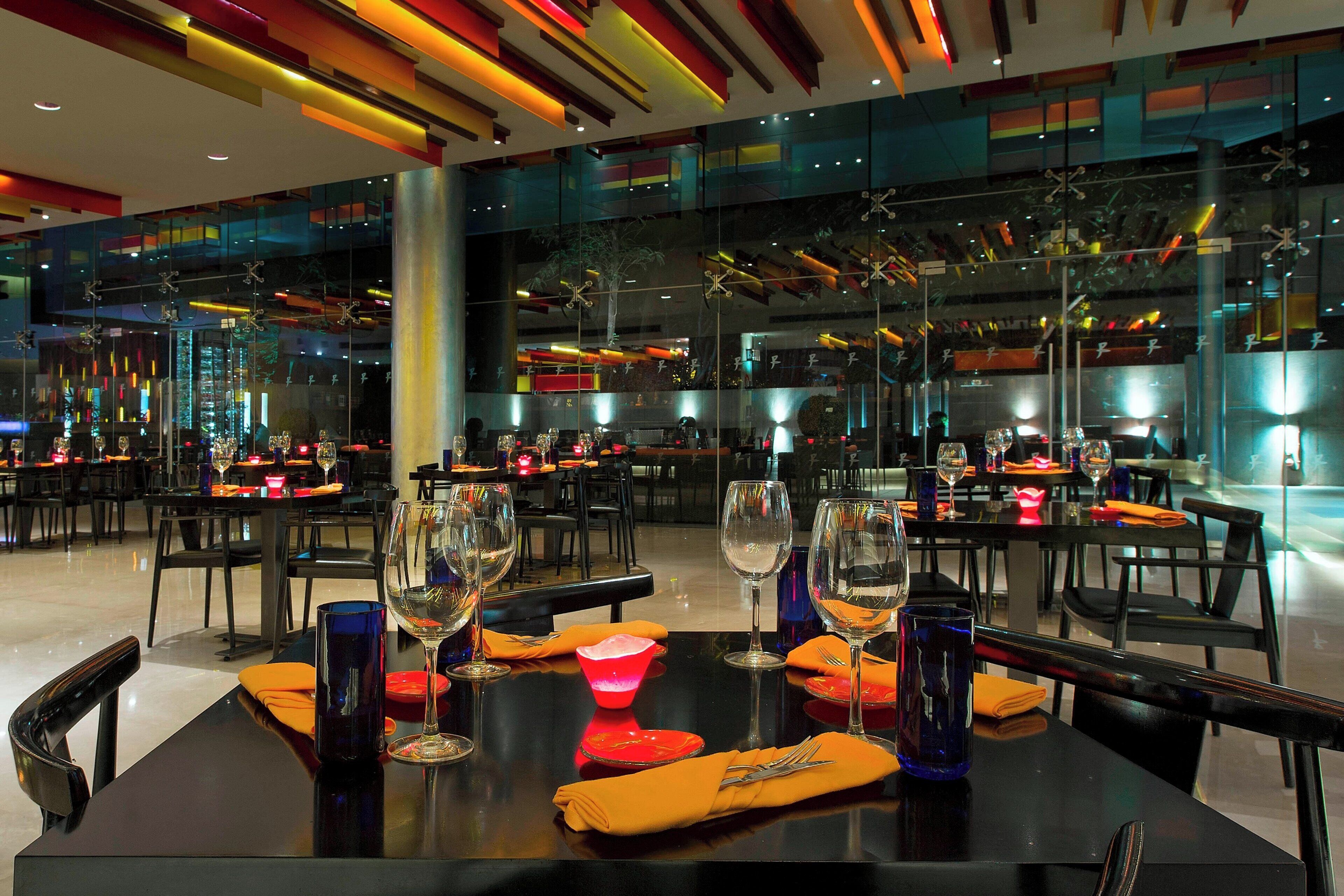 A modern restaurant with tables set for dining, featuring glass partitions and contemporary lighting.