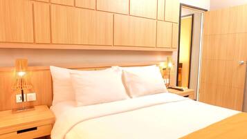 A hotel room with a wooden headboard, a bed with white bedding, a nightstand with a lamp, and a wardrobe.