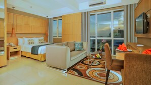 Habitación de hotel con cama, sofá, zona de comedor y un amplio ventanal con vistas a la ciudad.