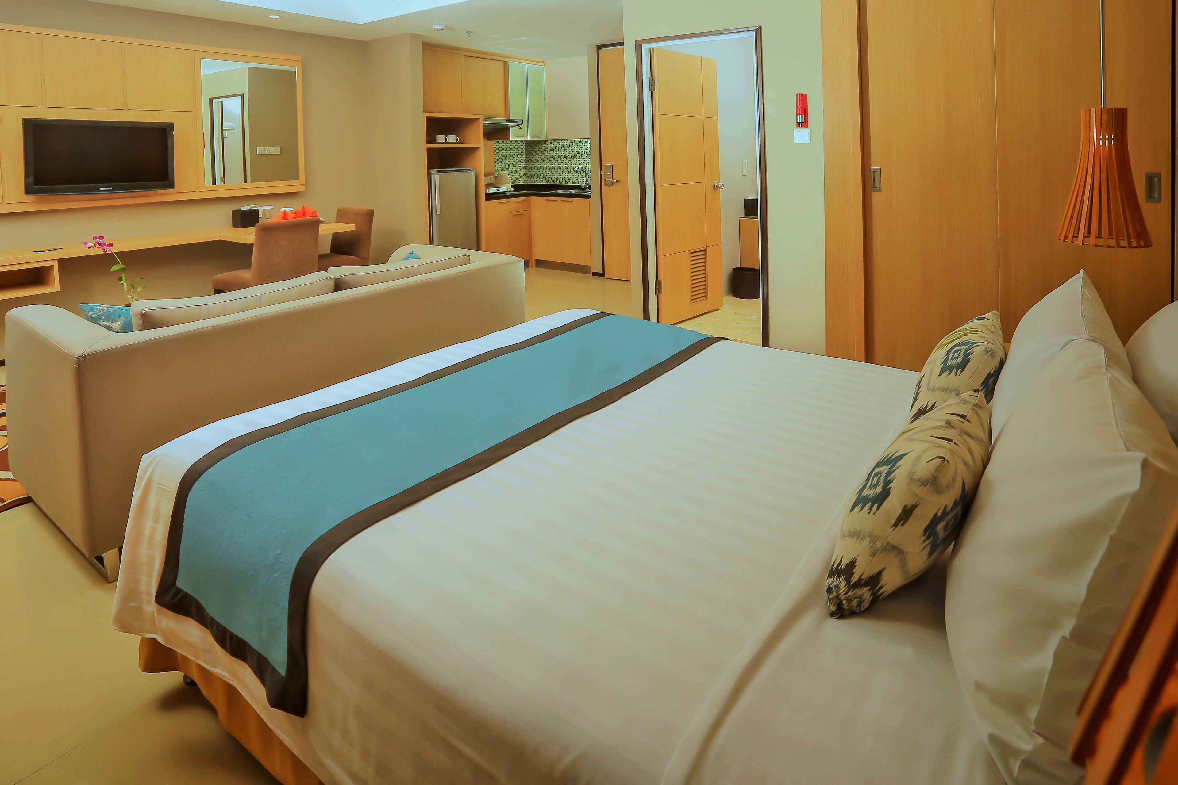A hotel room with a large bed, a sofa, a TV, a kitchenette, and a bathroom.
