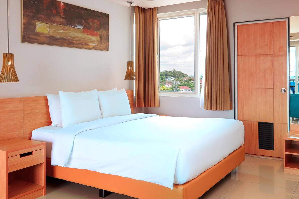 A hotel room with a bed, bedside table, and a window with curtains.