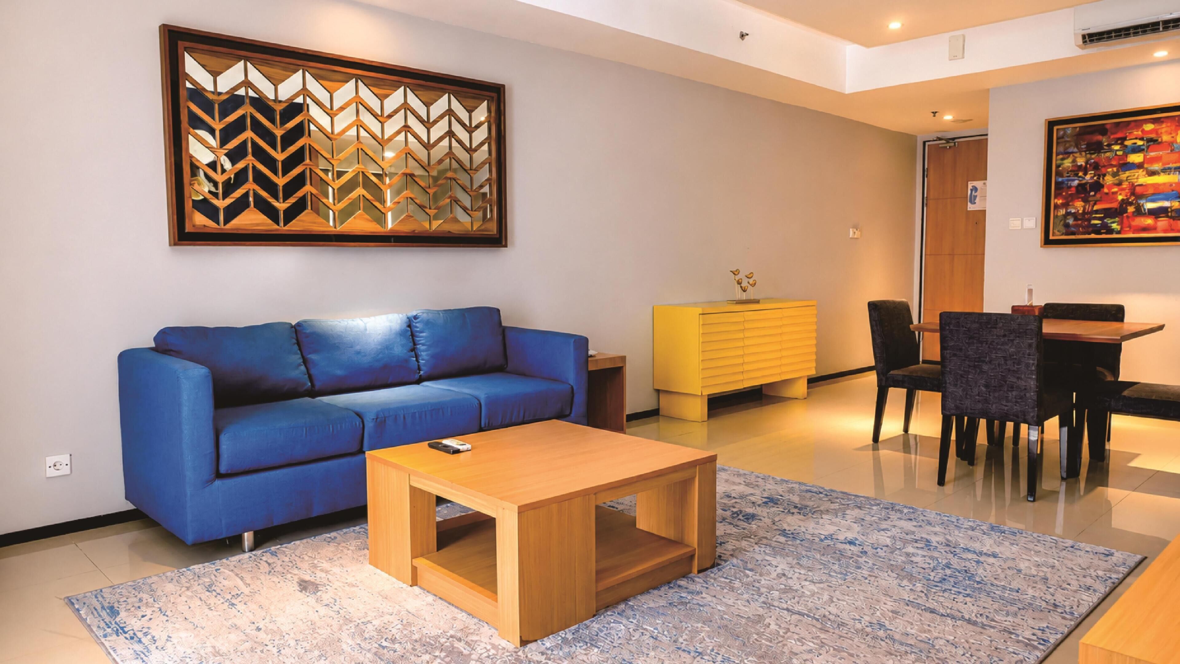 A modern living room with a blue sofa, wooden coffee table, and a yellow cabinet.