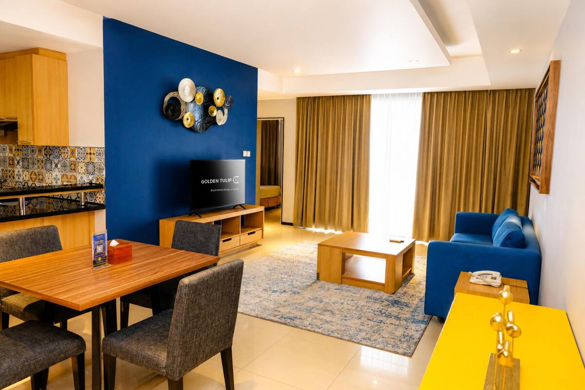 A modern living room with a blue accent wall, a wooden dining table, a blue sofa, and a television.