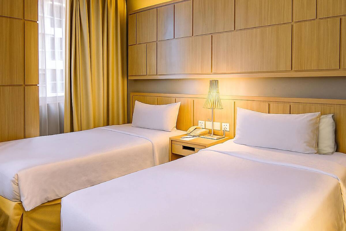 A hotel room with two beds, a nightstand with a lamp, and a wooden headboard.