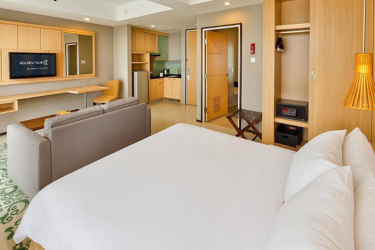 A hotel room with a large bed, a TV, a kitchenette, and a bathroom.