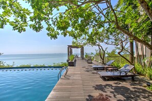 An infinity pool with a wooden deck, lounge chairs, and a view of the sea. - Golden Tulip Balikpapan Hotel & Suites (Balikpapan)