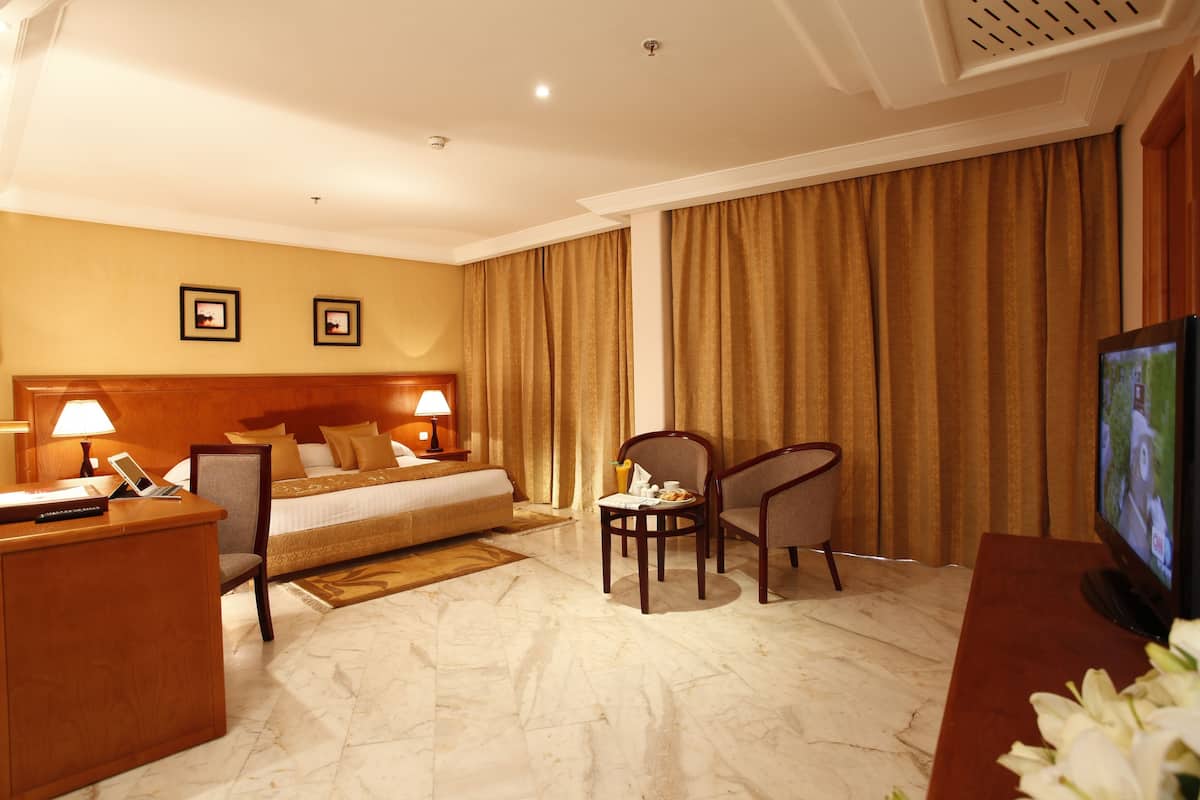 A hotel room with a bed, desk, chairs, a television, and a lamp.