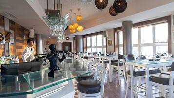 A modern dining area with glass tables, white chairs, and a bartender at the bar.
