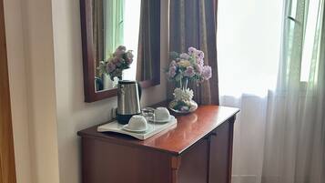 Un escritorio de madera con un espejo, una cafetera, tazas y un florero con flores.