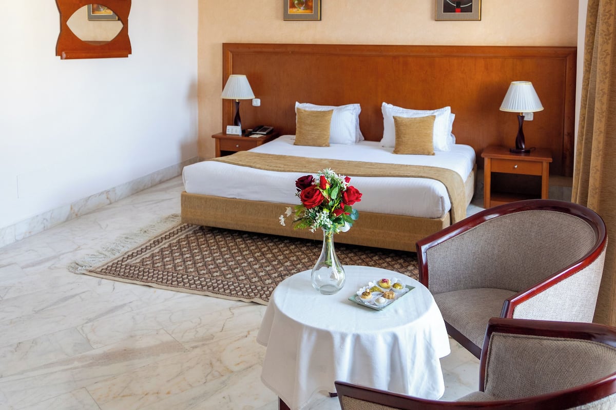 A hotel room with a large bed, two bedside tables, a small round table with a vase of flowers, and two chairs.