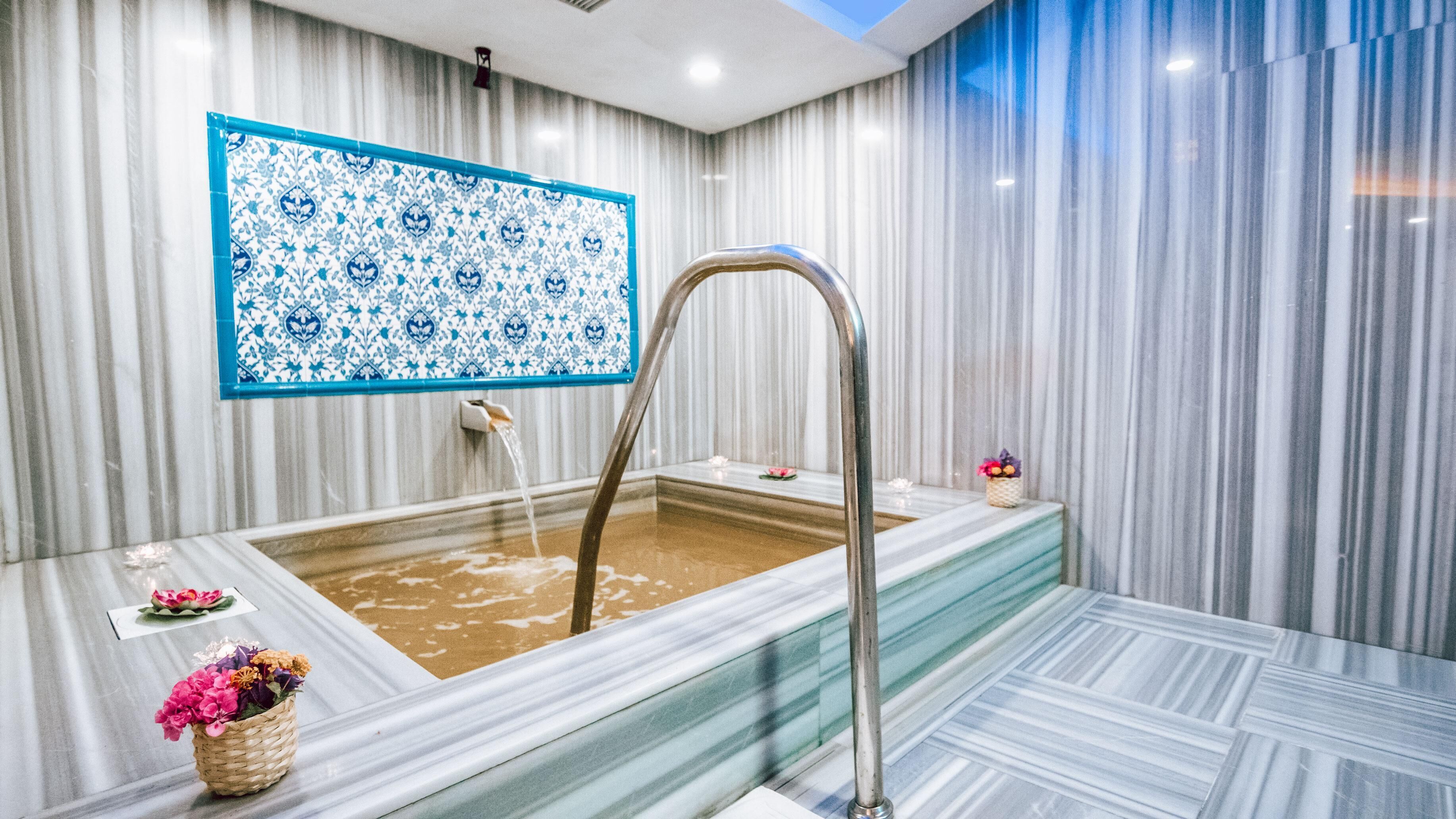Un baño moderno con una bañera de mármol, pared con estampado azul y blanco, y una pequeña cesta decorativa con flores.