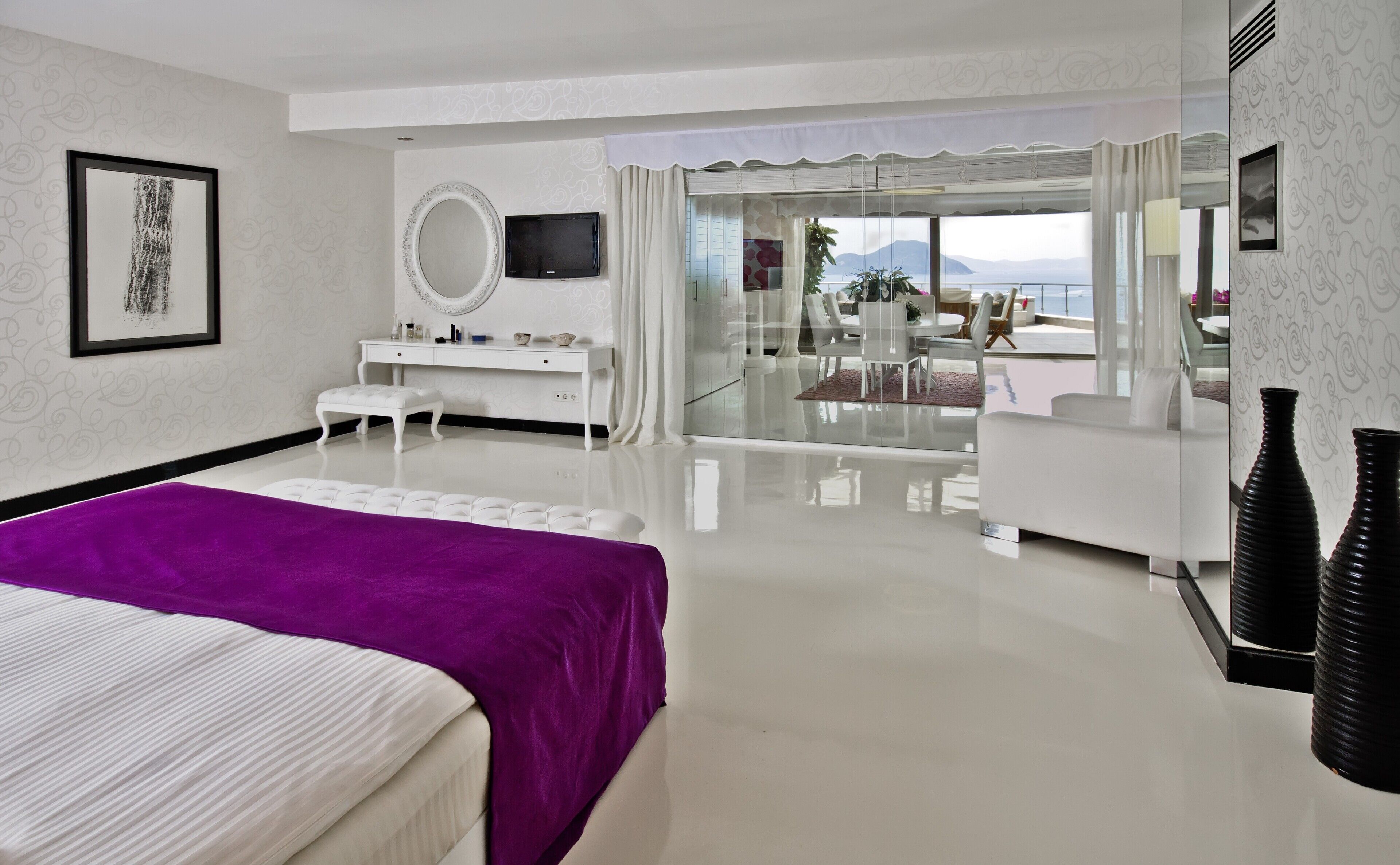 Una habitación de hotel moderna con una cama grande, una tocador con espejo, una televisión y un balcón con vista al mar.