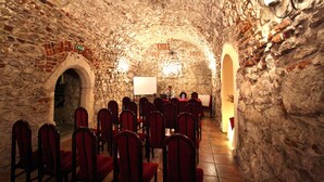 A stone-walled room with red chairs arranged in rows, a whiteboard, and a person at a table. - Hotel Wit Stwosz (Kraków)