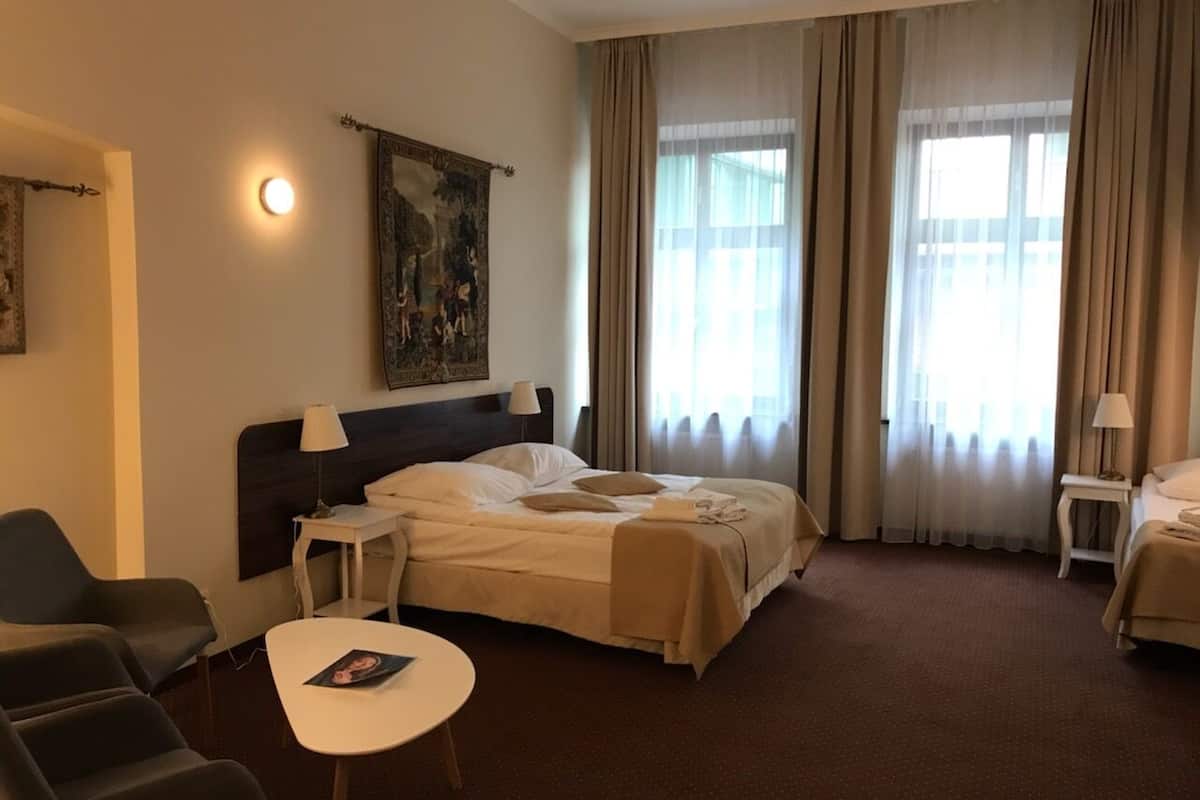 A hotel room with a bed, two chairs, a small table, a lamp, and a painting on the wall.