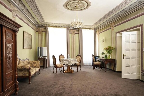 A room with a chandelier, a dining table with chairs, a sofa, a cabinet, and a door. - Hotel Wit Stwosz (Kraków)