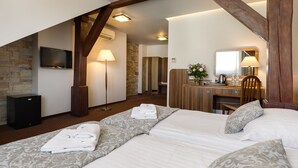 A hotel room with a bed, a desk, a chair, a TV, and a stone wall. - Hotel Wit Stwosz (Kraków)