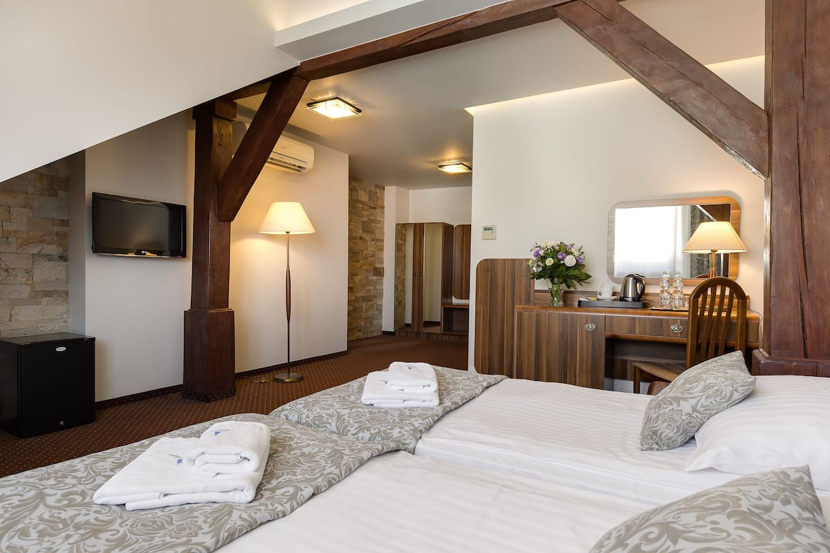 A hotel room with a bed, a desk, a chair, a TV, and a stone wall.
