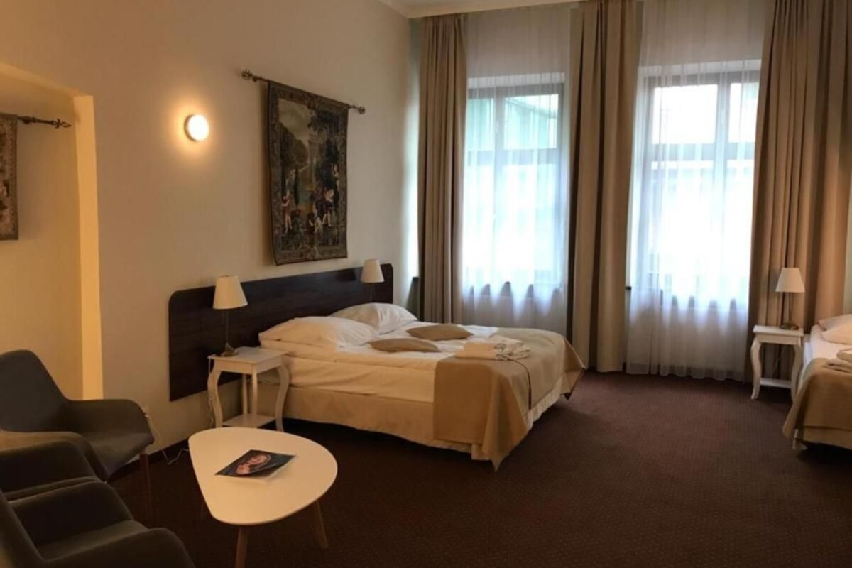 Una habitación de hotel con cama, una mesita, una silla, una lámpara y un cuadro en la pared.
