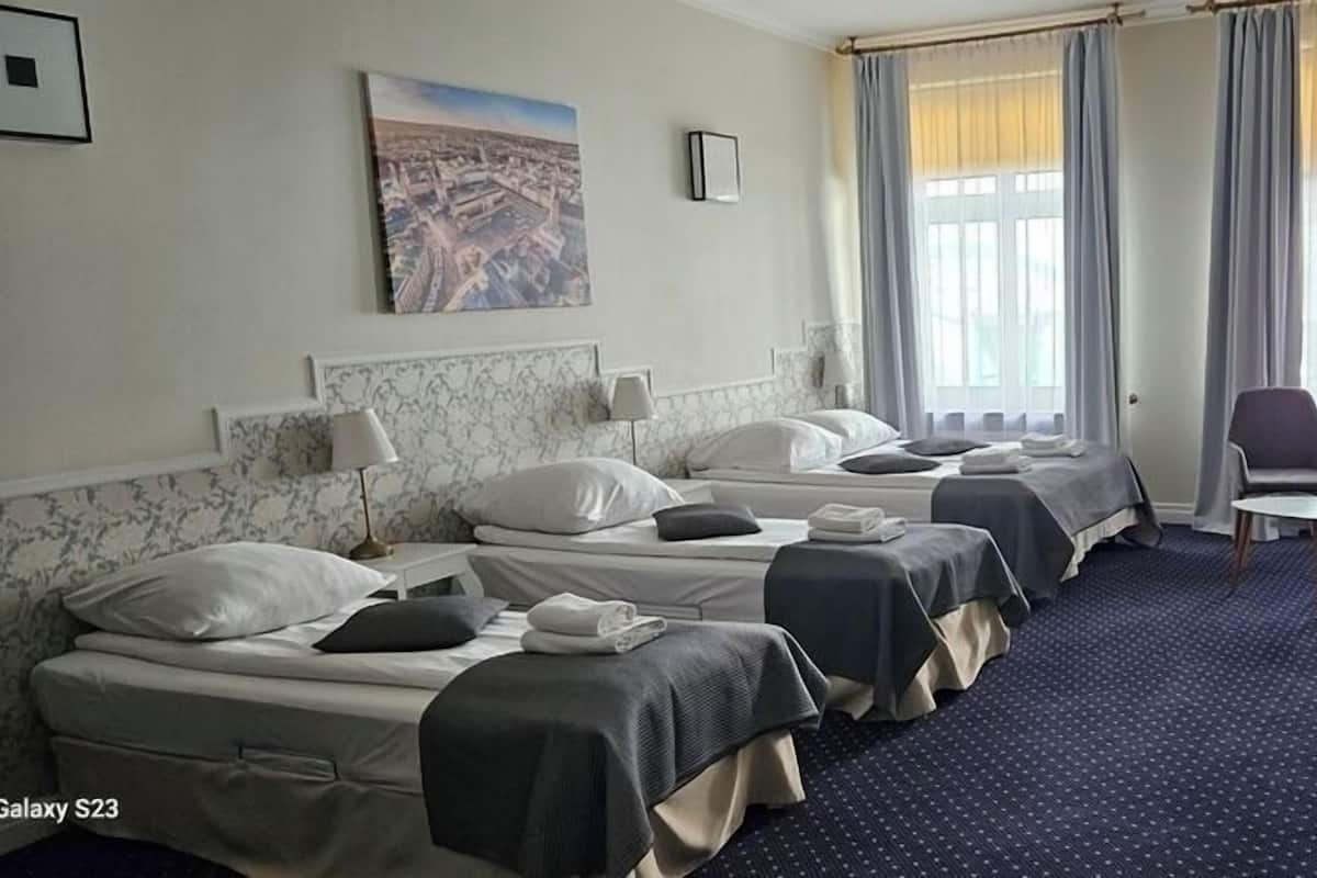 A hotel room with three beds, a desk, a chair, and a large window with curtains.