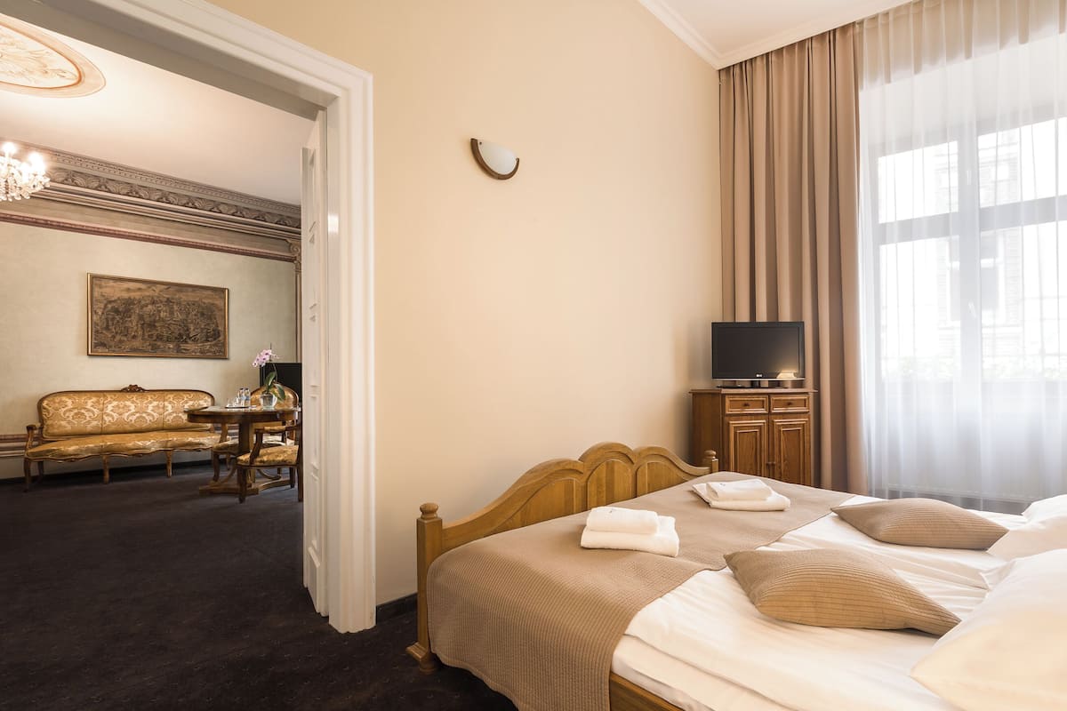 A hotel room with a bed, a television, a sofa, and a painting on the wall.