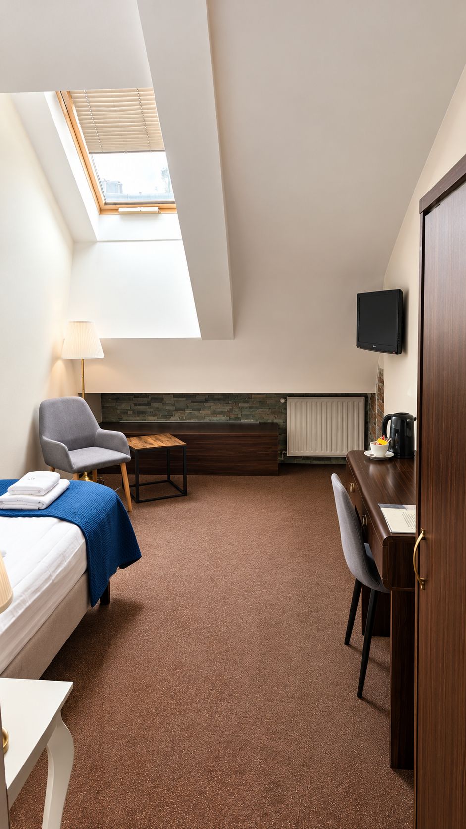 Una habitación de hotel con cama, escritorio, silla, televisor y tragaluz.