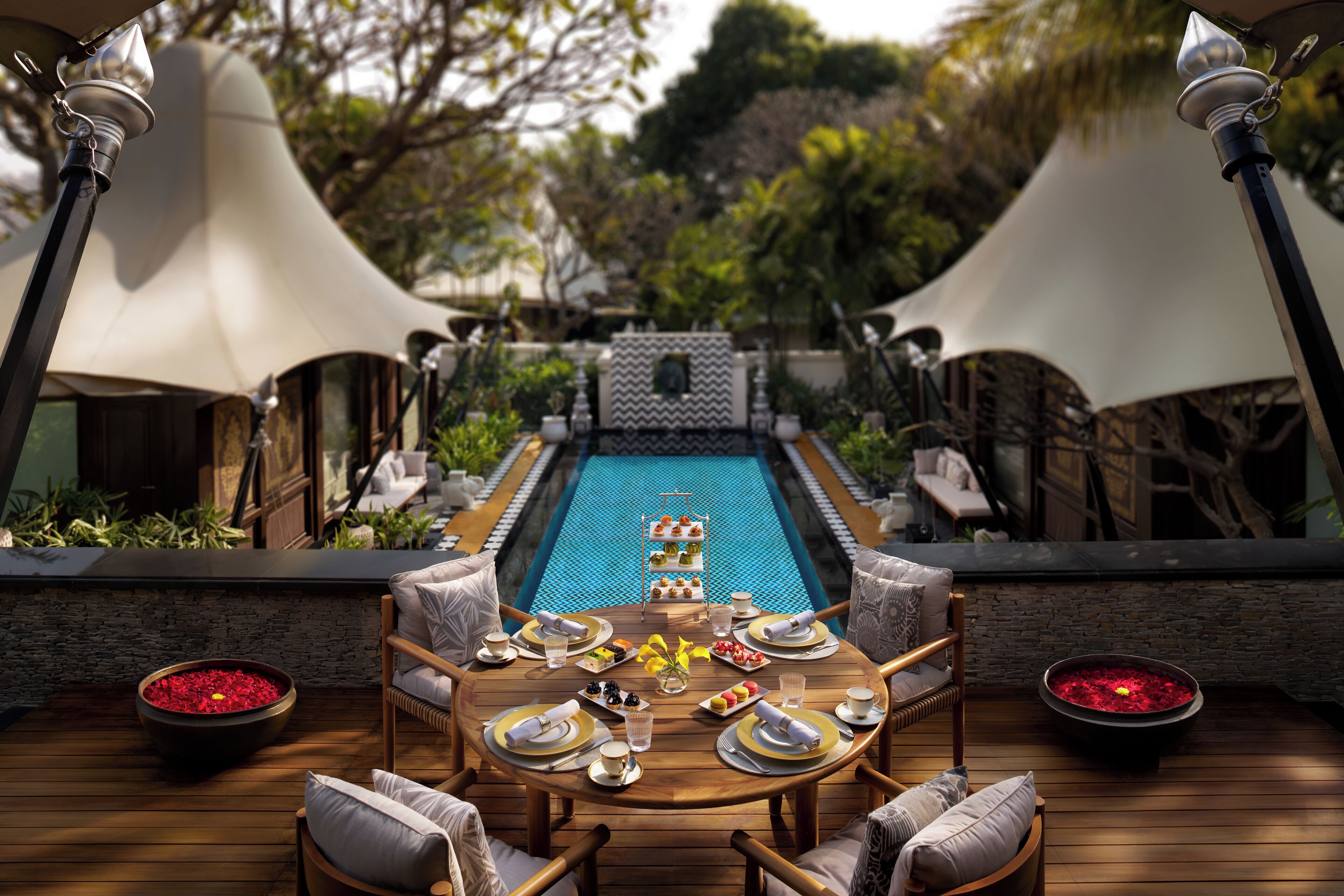 An outdoor dining area with a pool, wooden furniture, and a buffet setup.