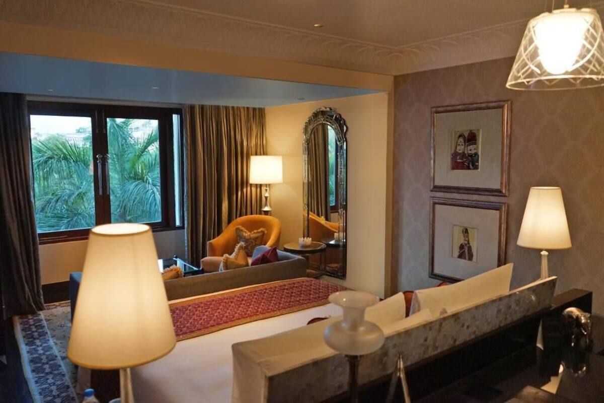 A hotel room with a large window, a sofa, a mirror, and two lamps.