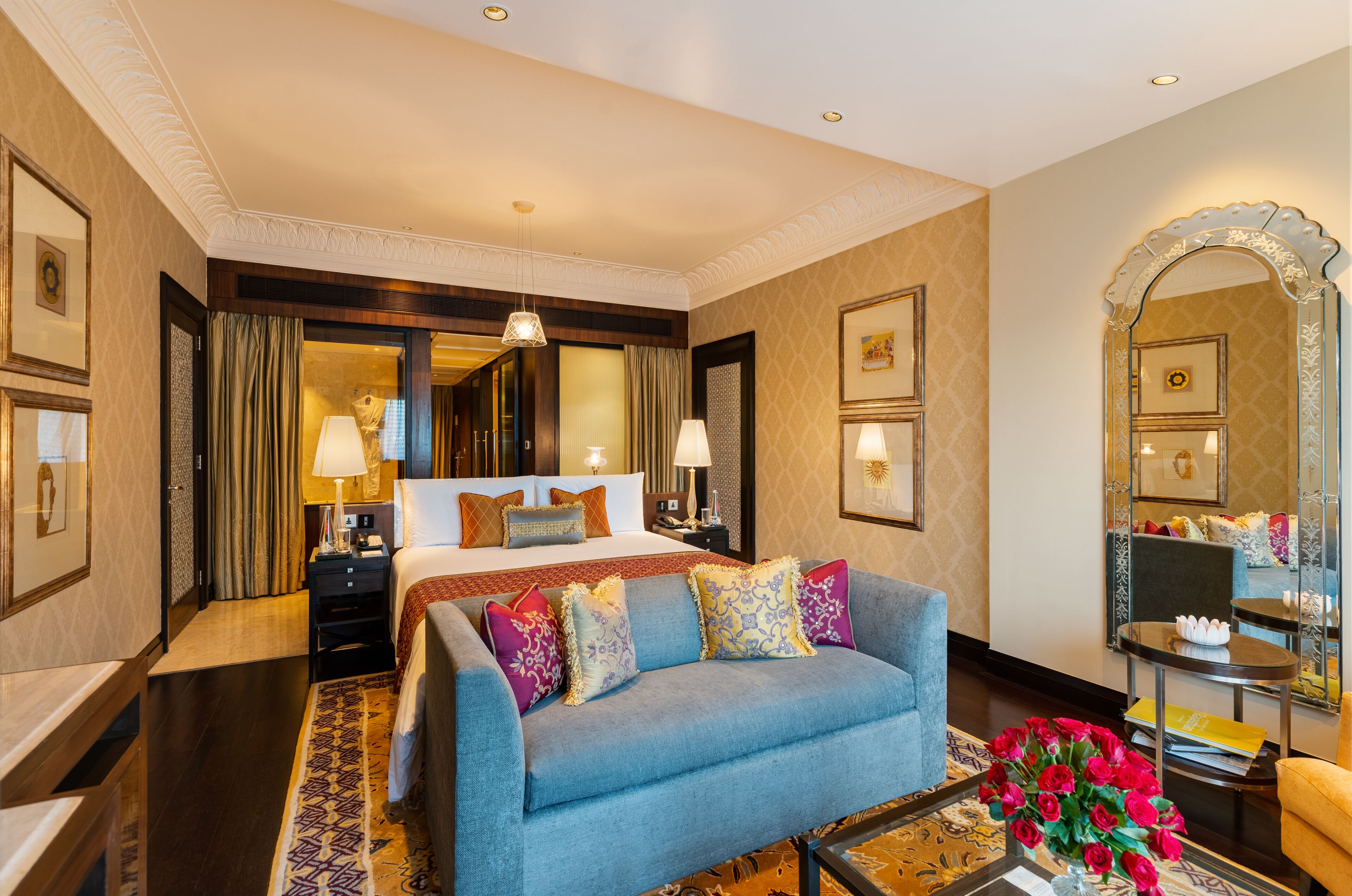A hotel room with a large bed, a sofa, a small table, and a mirror.
