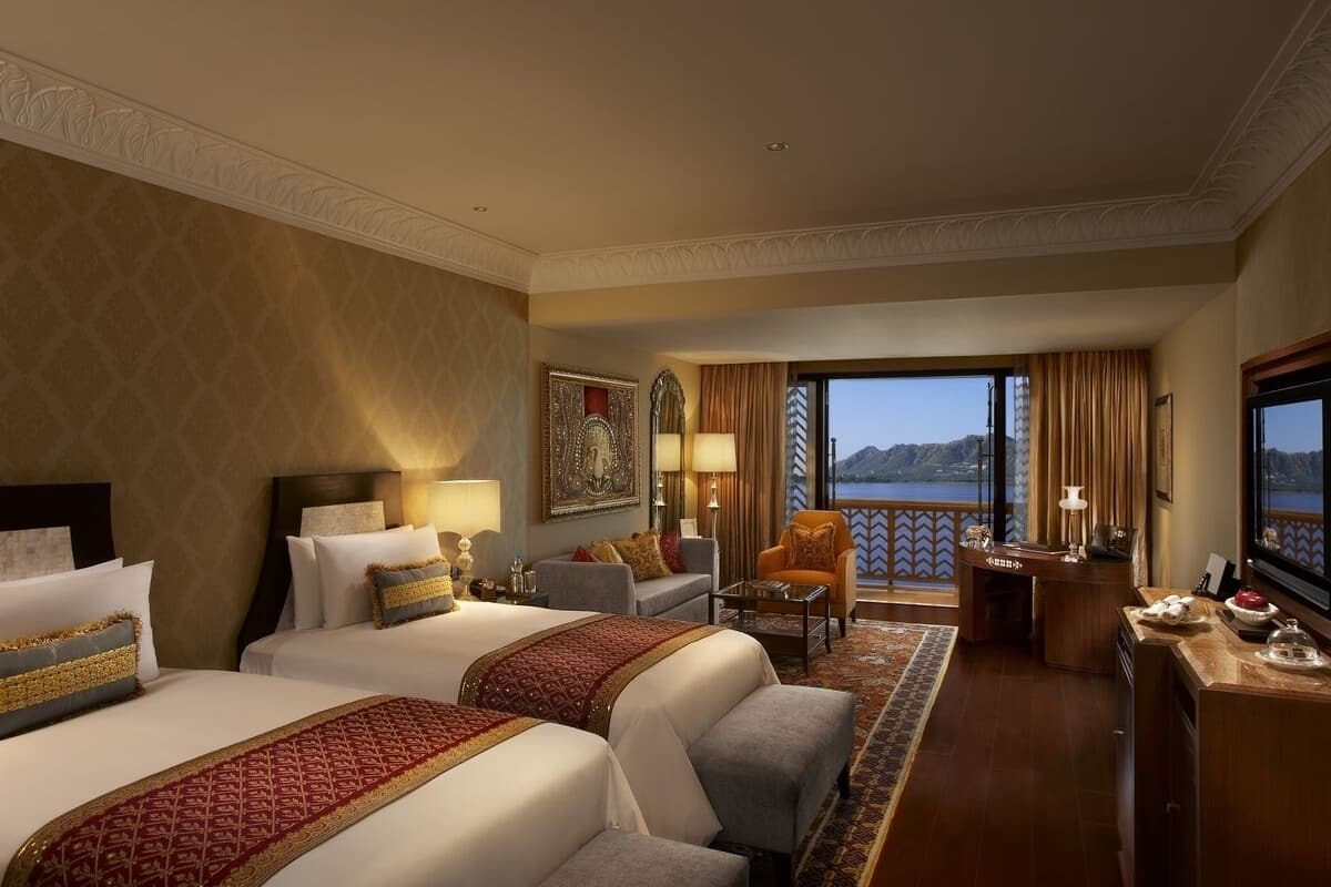 Ein Hotelzimmer mit zwei Betten, einem Sofa, einem Schreibtisch und Blick auf ein Gewässer.