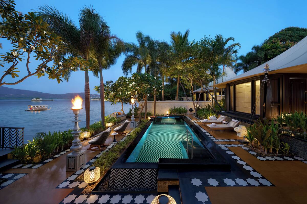 A pool area with lounge chairs, a water feature, and a view of the sea.