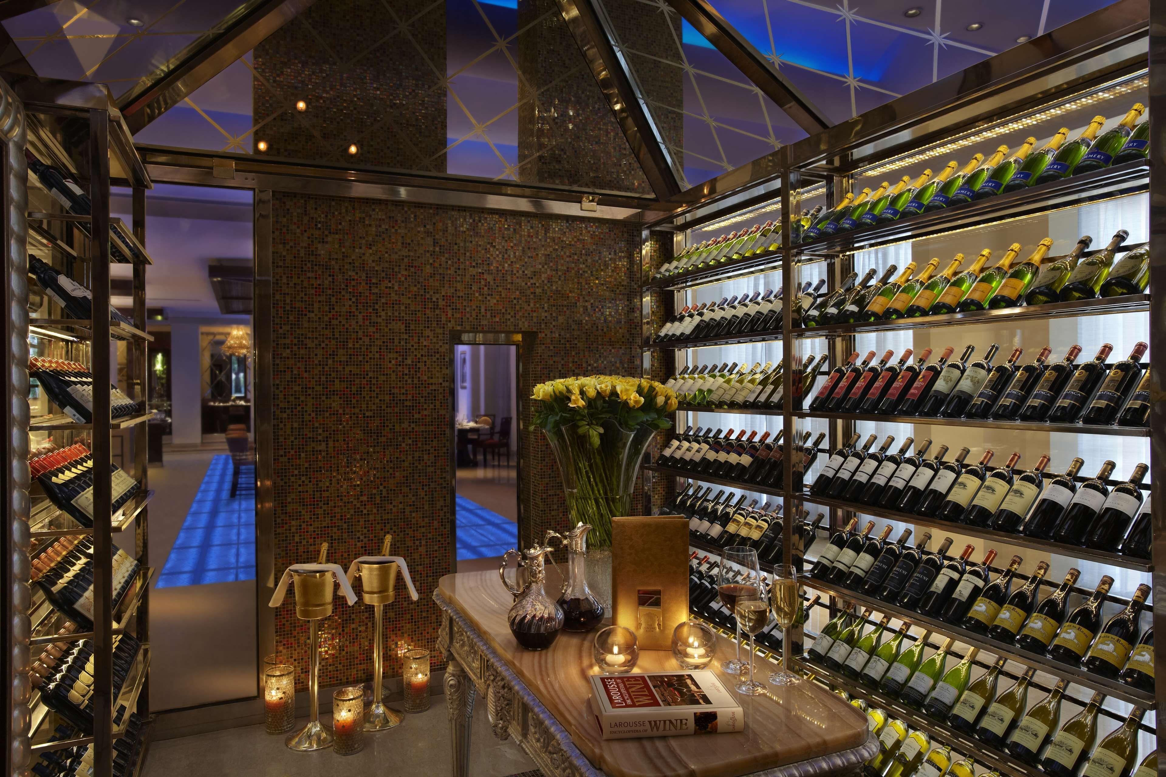 A wine cellar with shelves of wine bottles, a wooden counter with candles, and a vase of yellow flowers.
