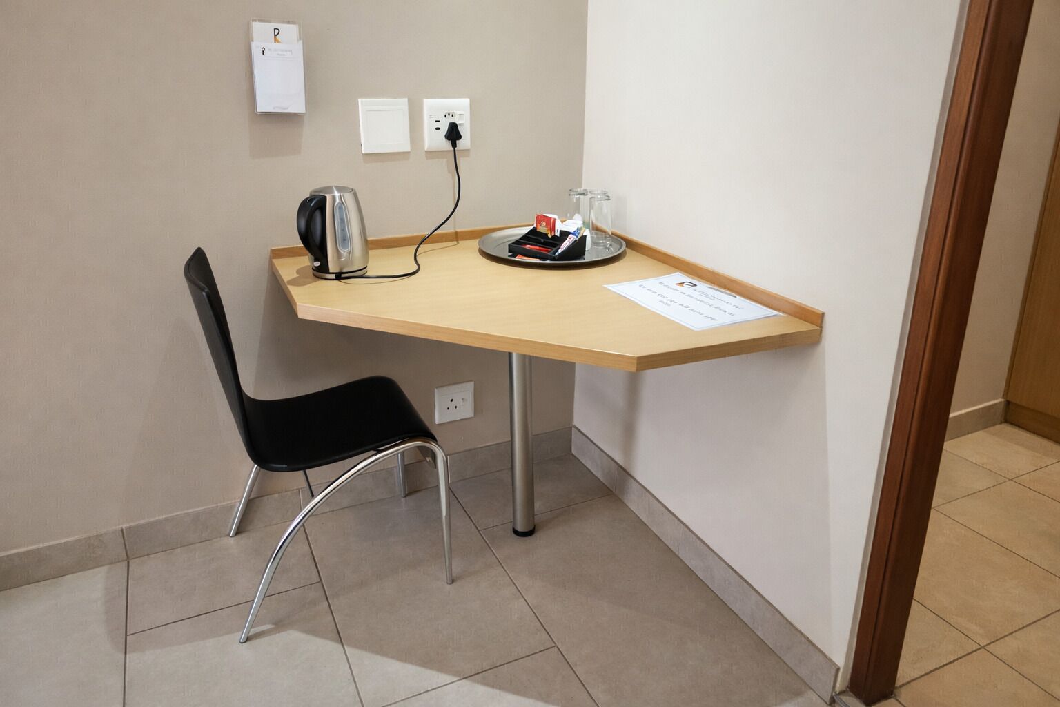 A small office space with a desk, a chair, a kettle, and a glass of water.