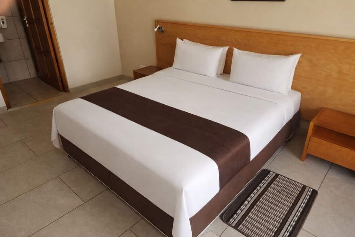 A hotel room with a large bed, wooden headboard, two bedside tables, and a patterned rug.