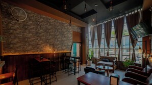 A modern bar area with a stone wall, wooden furniture, and large windows with curtains.