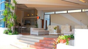 A modern indoor space with a staircase leading to a seating area, a kitchen in the background, and potted plants.