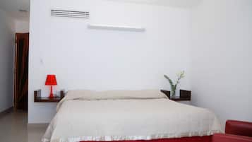 Un dormitorio con una cama, una lámpara roja, una mesita con un florero y una silla roja.