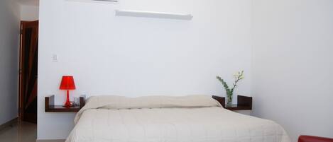 A bedroom with a bed, a red lamp, a small table with a vase of flowers, and a red chair.