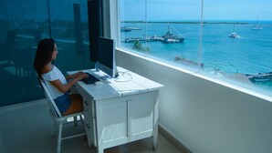A woman working at a desk by a large window with a view of the sea and boats.