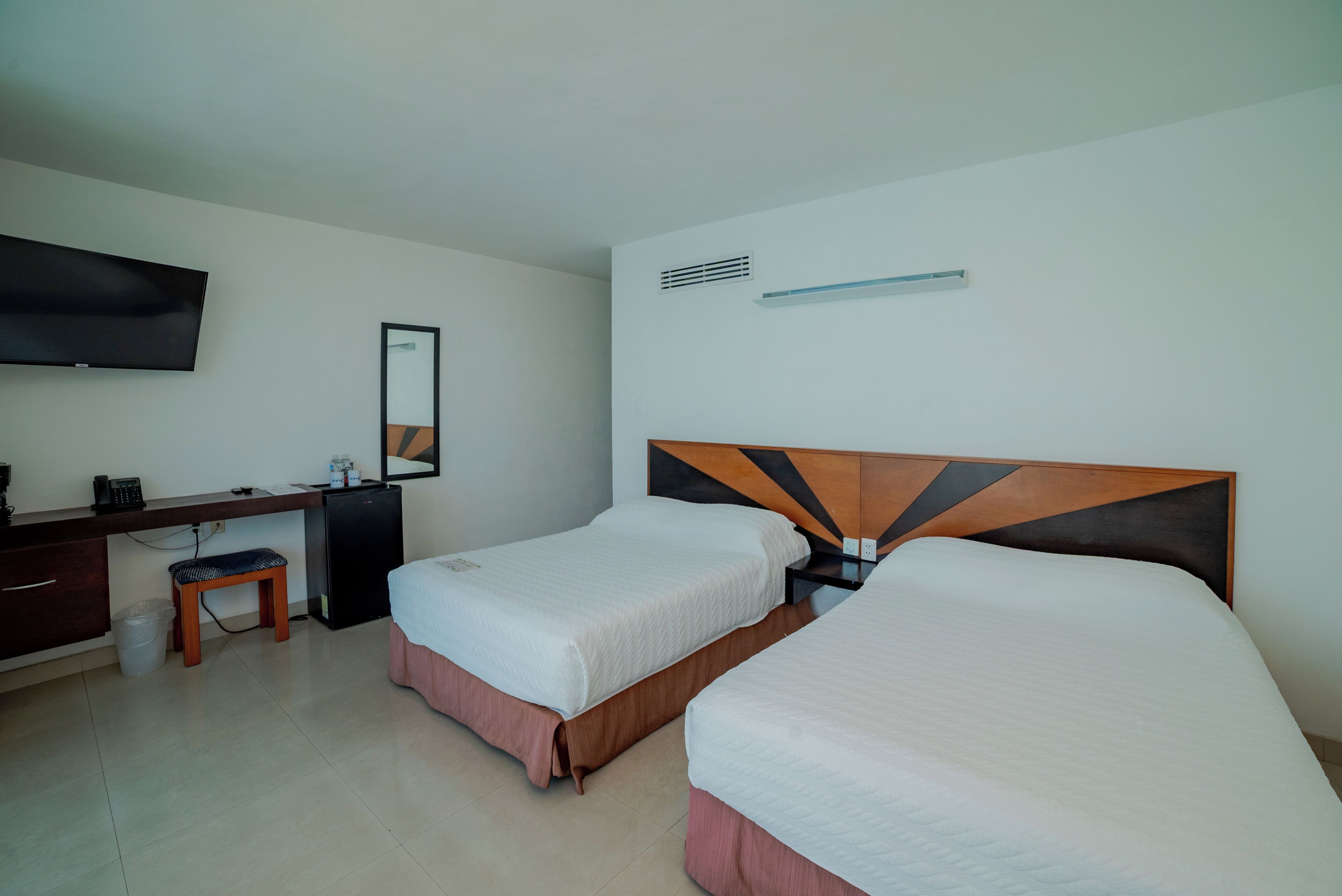 A hotel room with two beds, a desk, a chair, a TV, and a mirror.