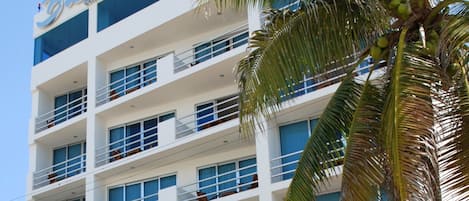 Un hotel de varios pisos con balcones, palmeras y coches aparcados.