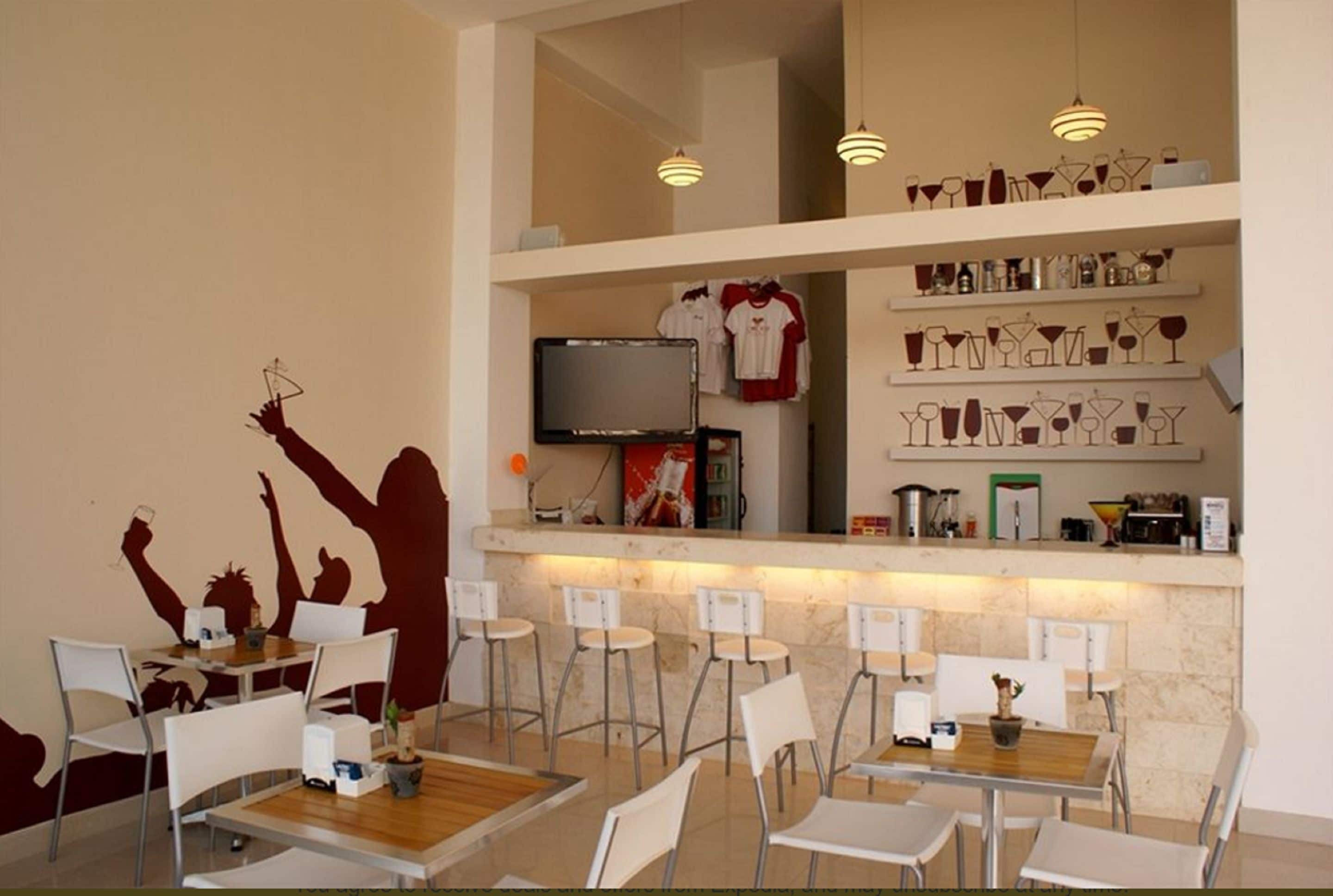 A restaurant with a bar area, white chairs, and a counter with shelves displaying glasses and bottles.